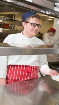 Catering student passing through dish from kitchen