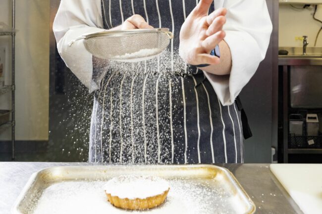 Catering student sieving icing sugar