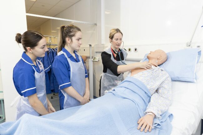 Health and care students and tutor practising on medical dummy