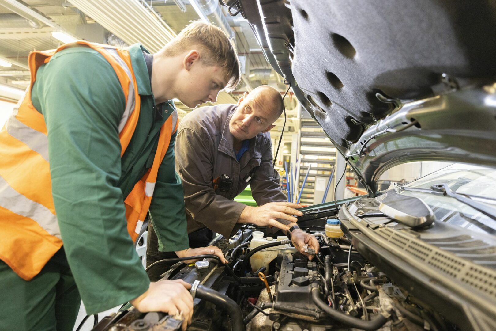 Motor vehicle student working on car engine with tutor