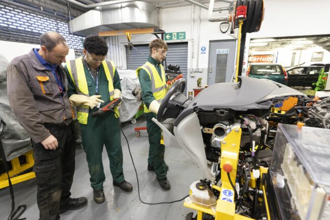 Motor vehicle students and tutor working on electric car