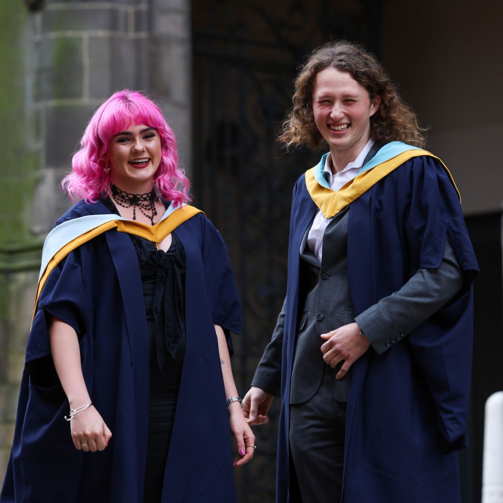 Two students smiling and laughing at their graduation ceremony