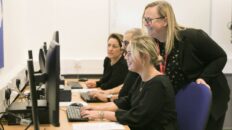 Adult learners at computers with teacher