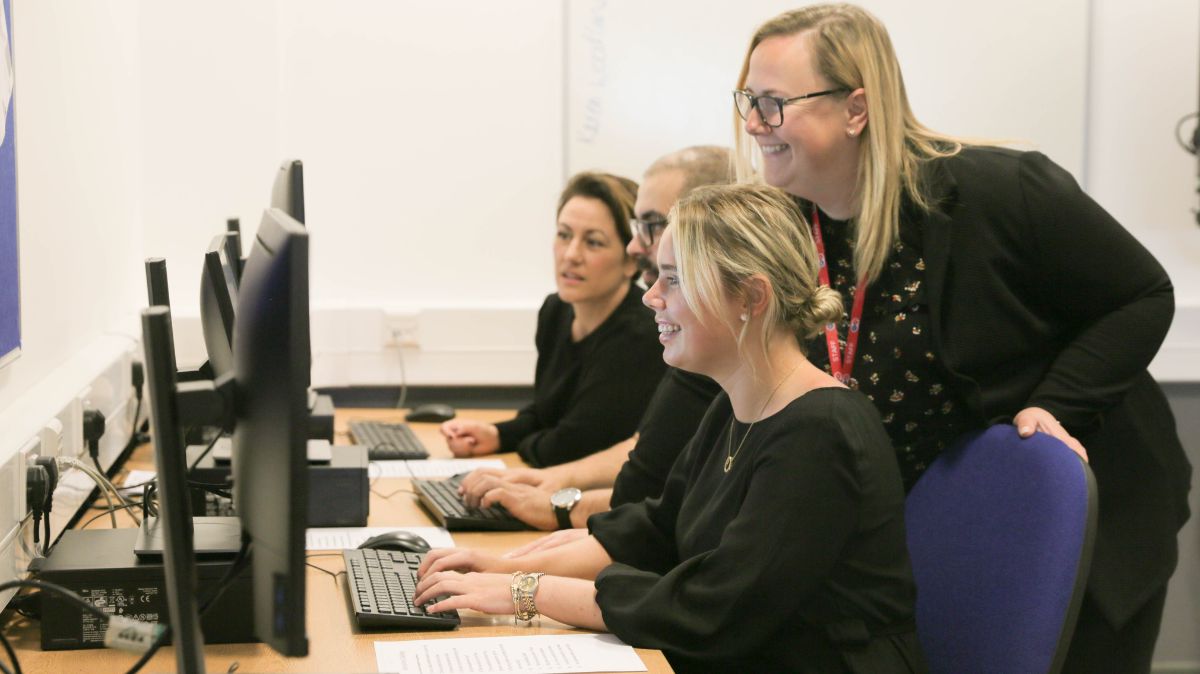 Adult learners at computers with teacher
