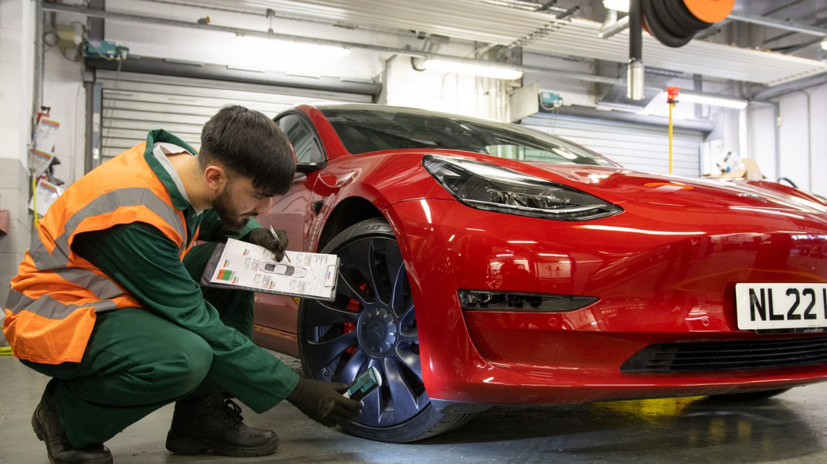 Student looking at wheel on red Tesla car